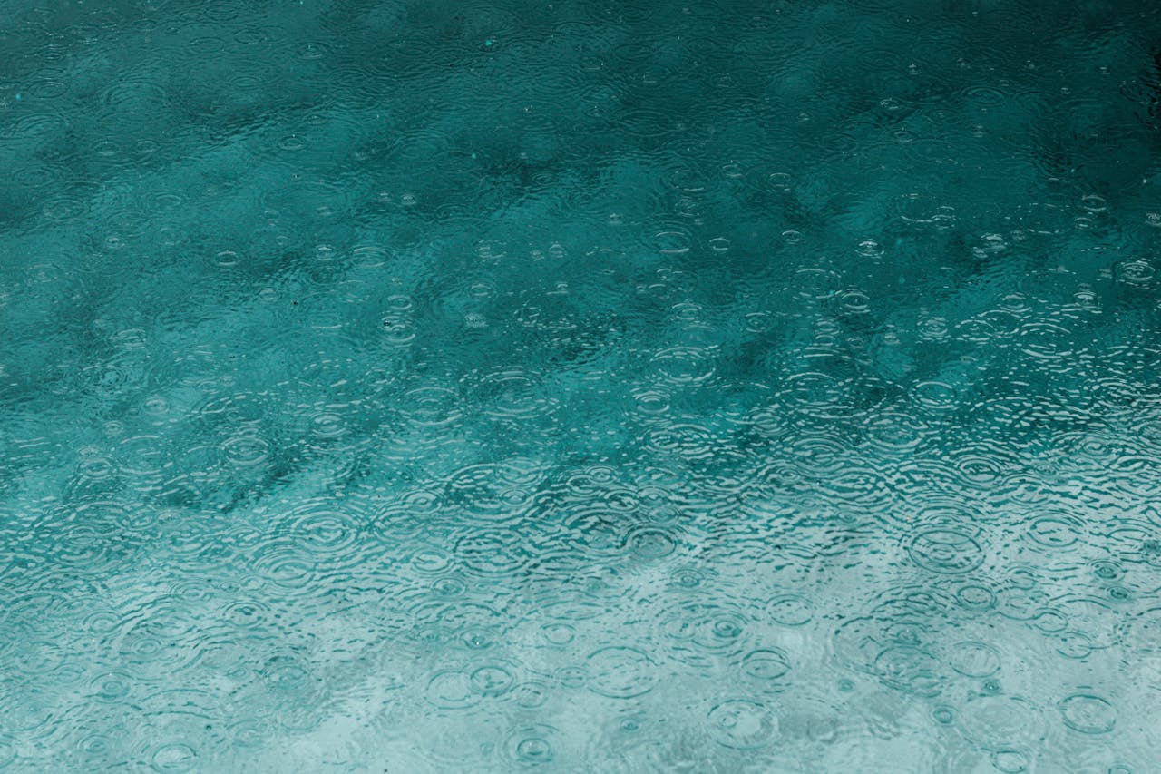 Serene teal water surface with ripples and raindrops, perfect for backgrounds.